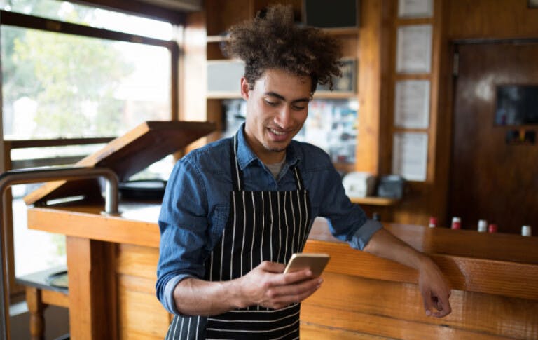 Man in apron in resturant checking his work hours on a phone.