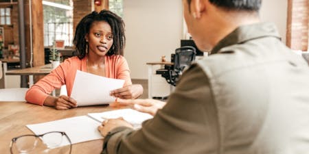 Disciplinary procedure A woman engages in a conversation with a man at a desk regarding a disciplinary procedure, highlighting a formal setting.