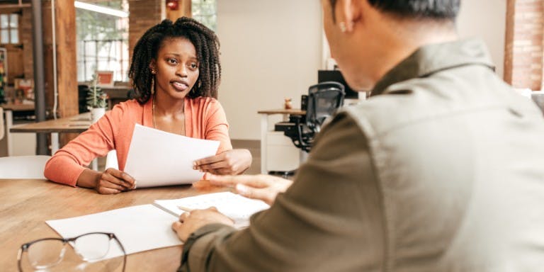 Disciplinary hearing A woman engages in a conversation with a man at a desk regarding a disciplinary procedure, highlighting a formal setting.