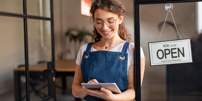 Woman smiling using a shift schedule maker on a tablet in her resturant.