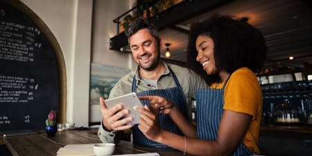 Two business owners looking at a tablet in their resturtant wokring out employee hours.