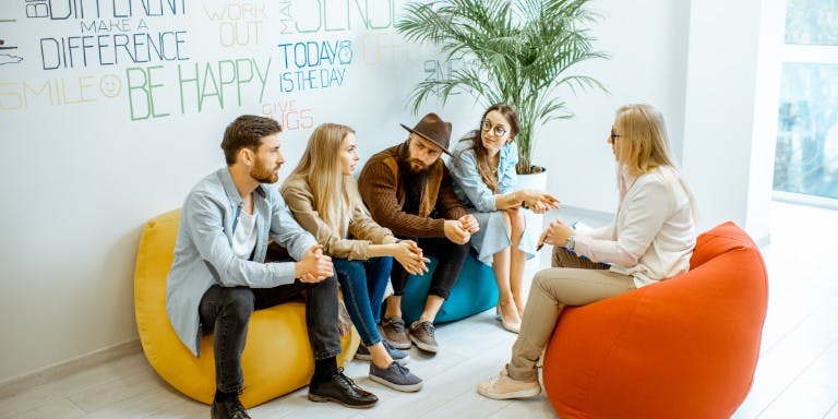 Four individuals seated on colorful bean bags in a modern office environment, engaged in conversation and collaboration.