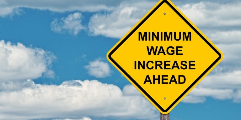 Graphic illustrating a minimum wage increase is coming with a yellow warning sign.
