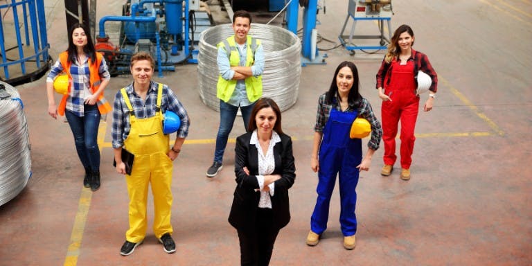 Group of temporary workers poses in front of a factory, highlighting their role in the manufacturing sector.