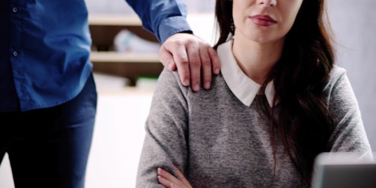 Women in a work environment with a male's hand on her shoulder.