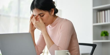 Work-related stress symptoms An employee sitting at a desk displaying signs of a headache, which is a physical symptom of work-related stress