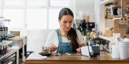 Coffee shop employee reviewing entering timesheets on a tablet.
