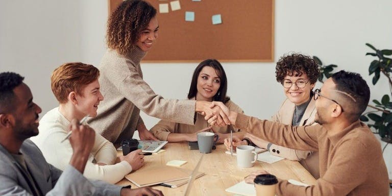 Individuals from various backgrounds shaking hands, representing teamwork and unity in a professional meeting setting