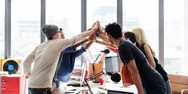 Office team members joyfully exchanging high fives, symbolising successful collaboration and strong teamwork among colleagues.