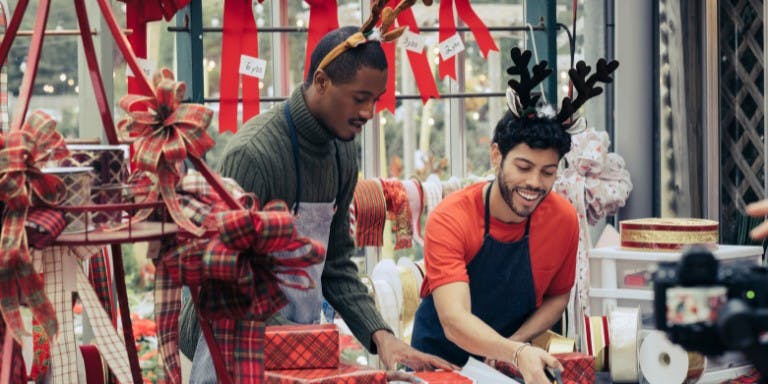 Two seasonal workers in a store, surrounded by festive Christmas decorations, preparing for the holiday shopping season.