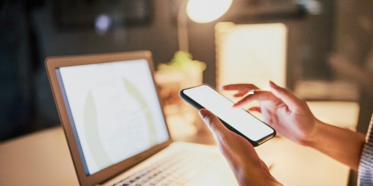 Social media in the workplace A person scrolling through their personal mobile device while working at a desk