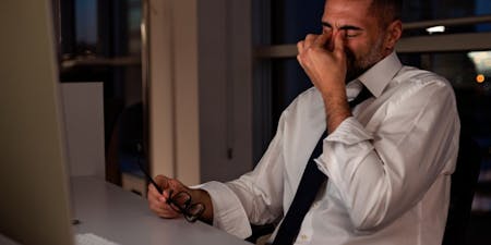 Night Shifts Male employee at desk working a night shift rubbing tired eyes