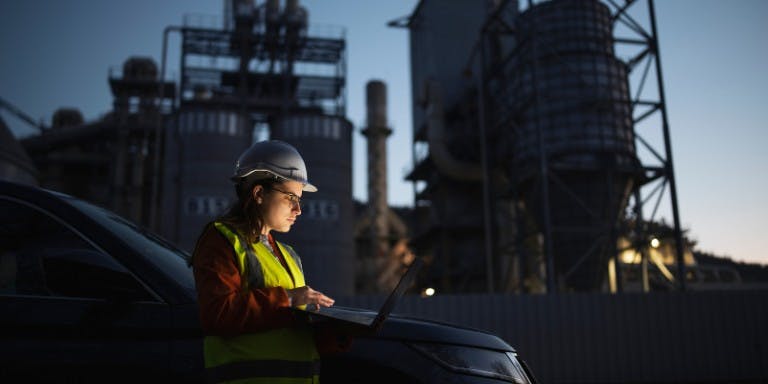 Night shift worker using health and safety software on a laptop at a factory