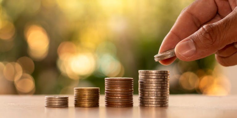 A hand adds coins to a stack, representing the financial implications of recent statutory pay rate increases.