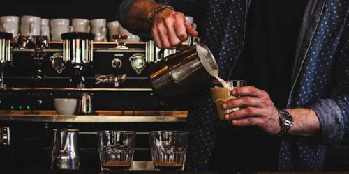 Male making a latte working a spilt shift in a coffee shop.