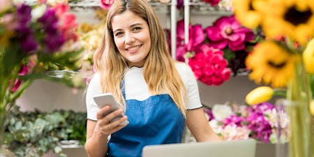 Female business owner happy using an HR management app on her phone in her flower shop.