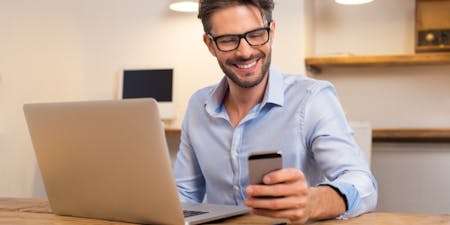 Male employer smiling using an HR management app from his home office.