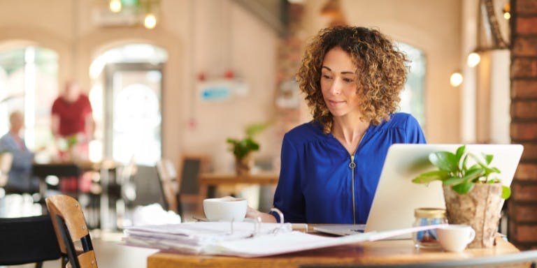 Female business owner reviewing flexible working requests at a table in her restaurant with a laptop and papers.