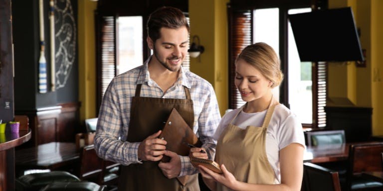 Male and female employees in aprons stand together at a table, embodying a friendly and professional atmosphere at work.