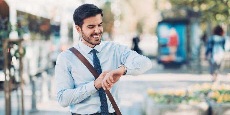 Male employee looking checking the time on his way to work, smiling.