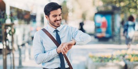 Flexible working hours Male employee looking checking the time on his way to work, smiling.