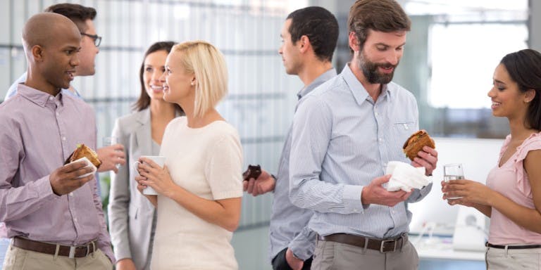 Group of employees chatting and gossiping in a breakroom with drinks and snacks.