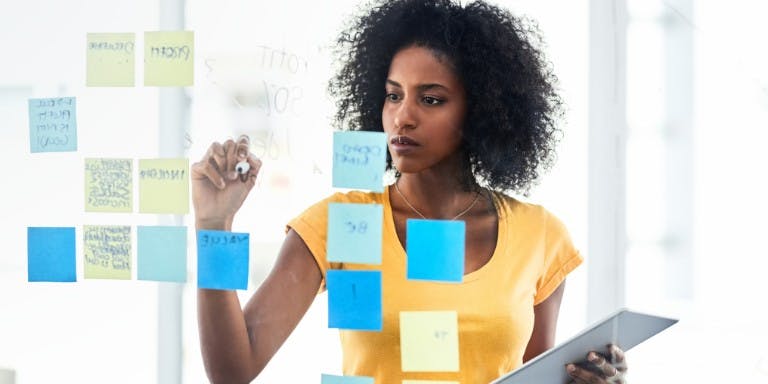 Employee goals and objectives A woman writes on sticky notes on a whiteboard, outlining employee goals and objectives in a collaborative workspace.