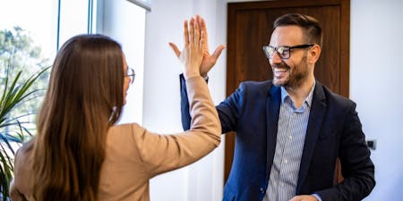 Employee goals and objectives A man and woman joyfully high five, illustrating the spirit of teamwork and the accomplishment of their performance goals.