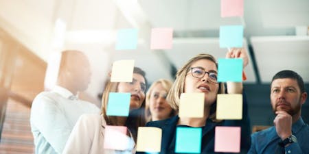 Performance Objectives eople gather around a wall filled with sticky notes, engaging in discussions about their performance objectives and strategies.