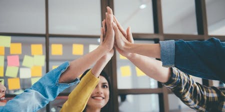 Performance Objectives Four colleagues in an office enthusiastically giving each other high fives, celebrating their performance objectives.