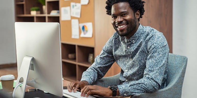 Smiling man at a desk with a computer,  drafting performance objectives for his business.