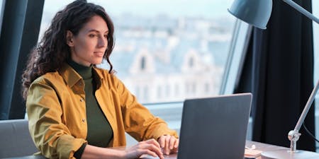 Woman seated at a desk, engaged with her laptop as she writes work performance objectives.