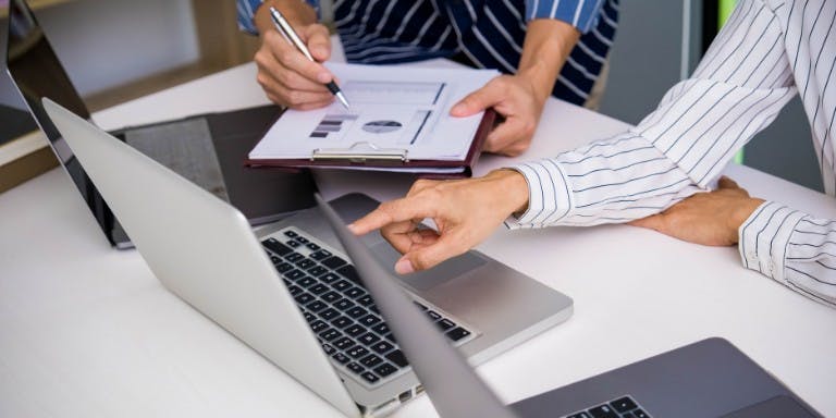 Two people working on laptops at a desk, concentrating on enhancing performance management practices with software.