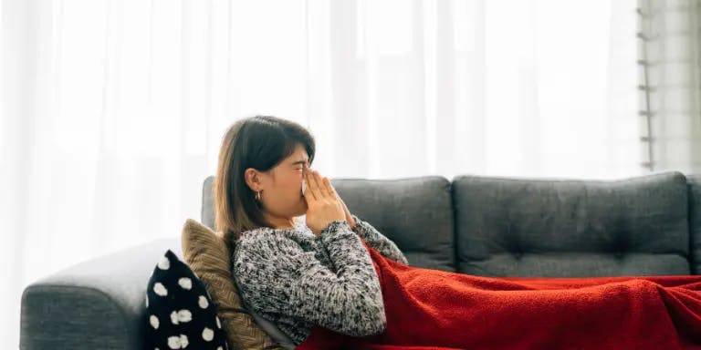 A woman off work, sick, on a sofa covered with a blanket, sneezing