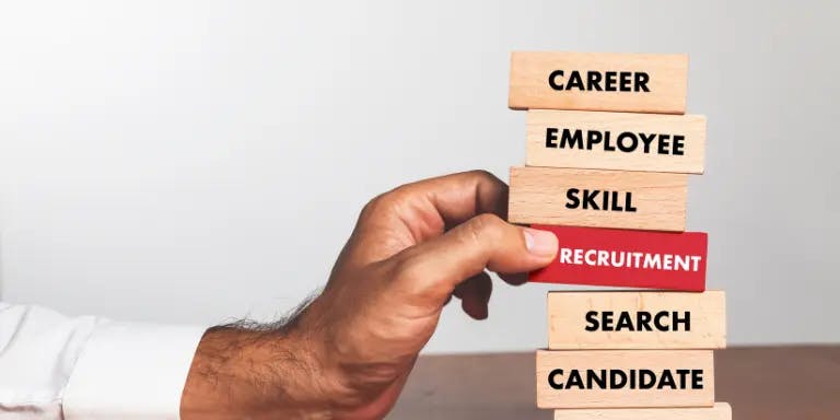 A hand of a man in a suit reaching for Jenga blocks labelled with various recruitment terms