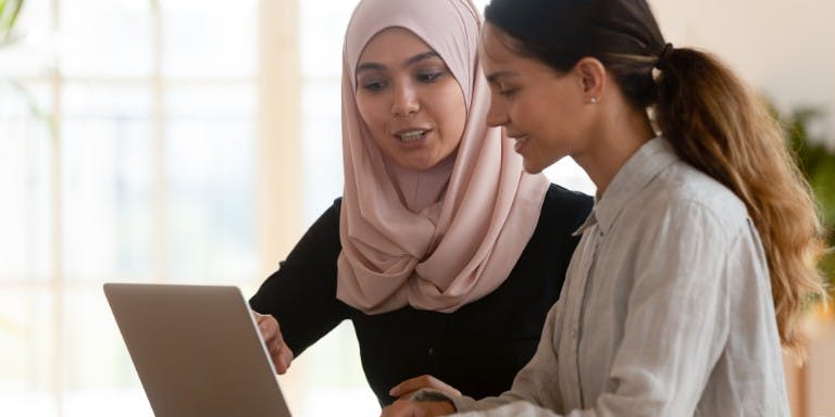 Two women collaborate over a laptop, engaged in a mentoring session at work.