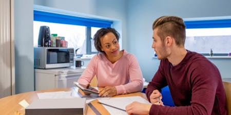 Employee performance reviews Female manager and male employee seated at a table, reviewing employee performance documents together.