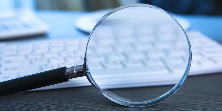 A magnifying glass on a desk in front of a keyboard