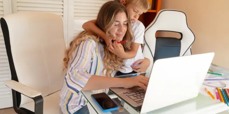 A woman working from home with her son hugging her