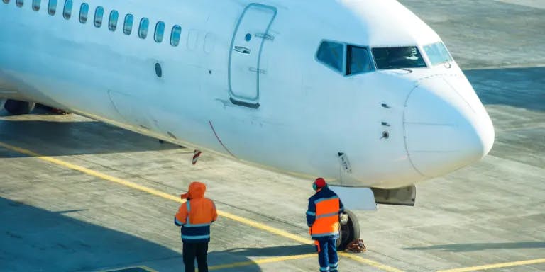 An aeroplane on a runway with two workers in high-vis jackets nearby
