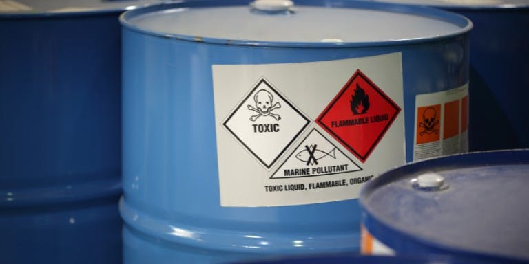 Multiple barrels featuring labels and signs, including hazardous substance symbols.