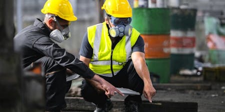 COSHH Two individuals in yellow safety vests and hard hats, demonstrating COSHH safety measures at a construction site.