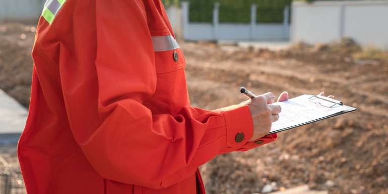 COSHH Assessment Individual in an orange jacket documenting COSHH assessments on a clipboard.