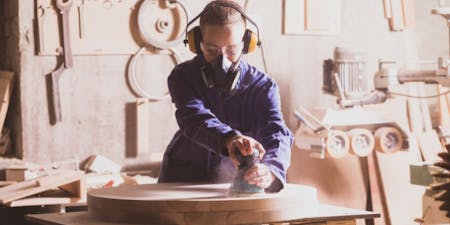 Woman sanding a wooden table, with hazardous substance dust present in the air.
