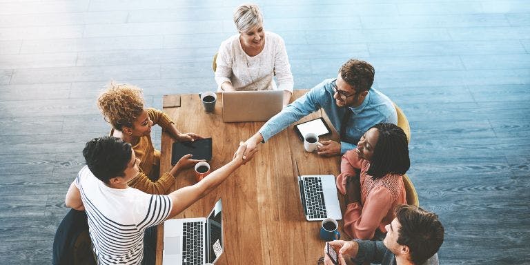 Employees sitting around a large desk agreeing on a workplace decision with a handshake across the table