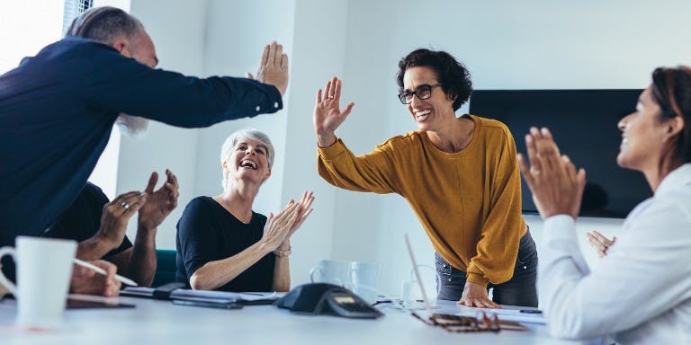 Employees in a meeting room high-fiving a co-workers career progression.