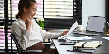 Career Progression Female employee reviewing promotion letter at a desk smiling and cheering.