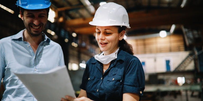 Woman and man with hard hats in a warehouse reviewing control measures for hazardous substances