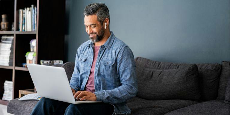 Man seated on a sofa using a laptop in a casual work setting, Man seated on a sofa using a laptop in a casual work setting,