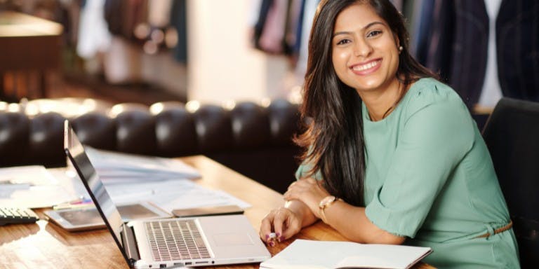 Female business owner creating an absence management policy at a desk with laptop, smiling.